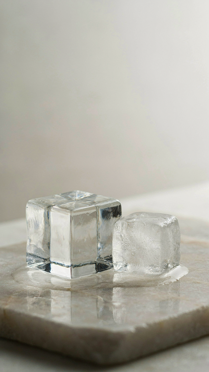 A large, clear ice block stands next to a small, cloudy ice cube.