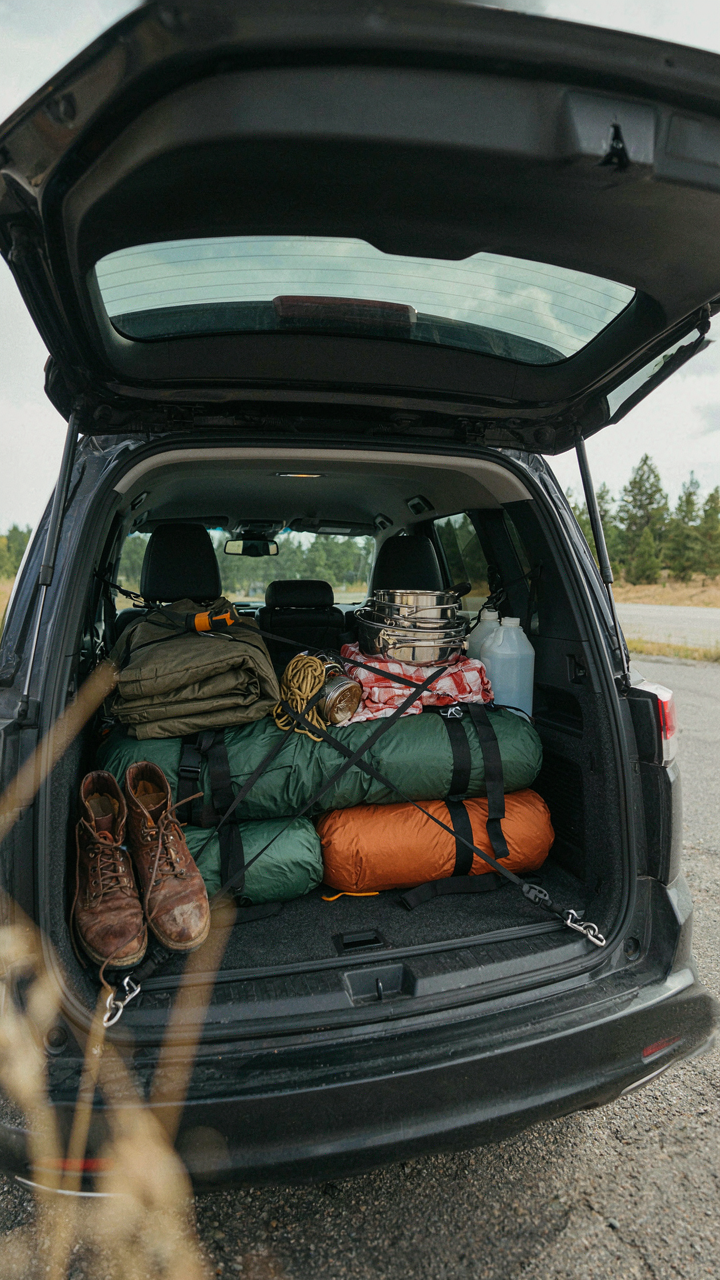 Camping gear in an SUV trunk is tightly packed and secured with bungee cords.