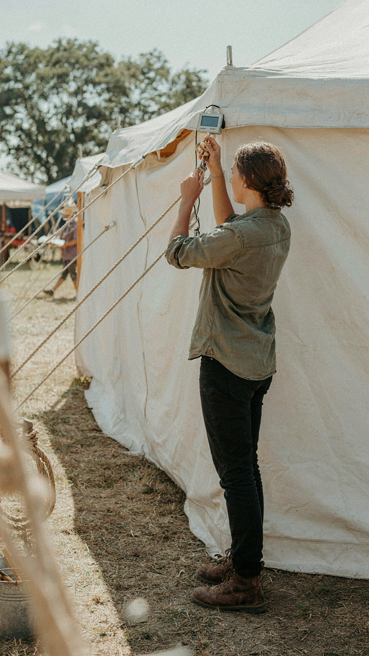 A person adjusts tent vents using a weather monitor.