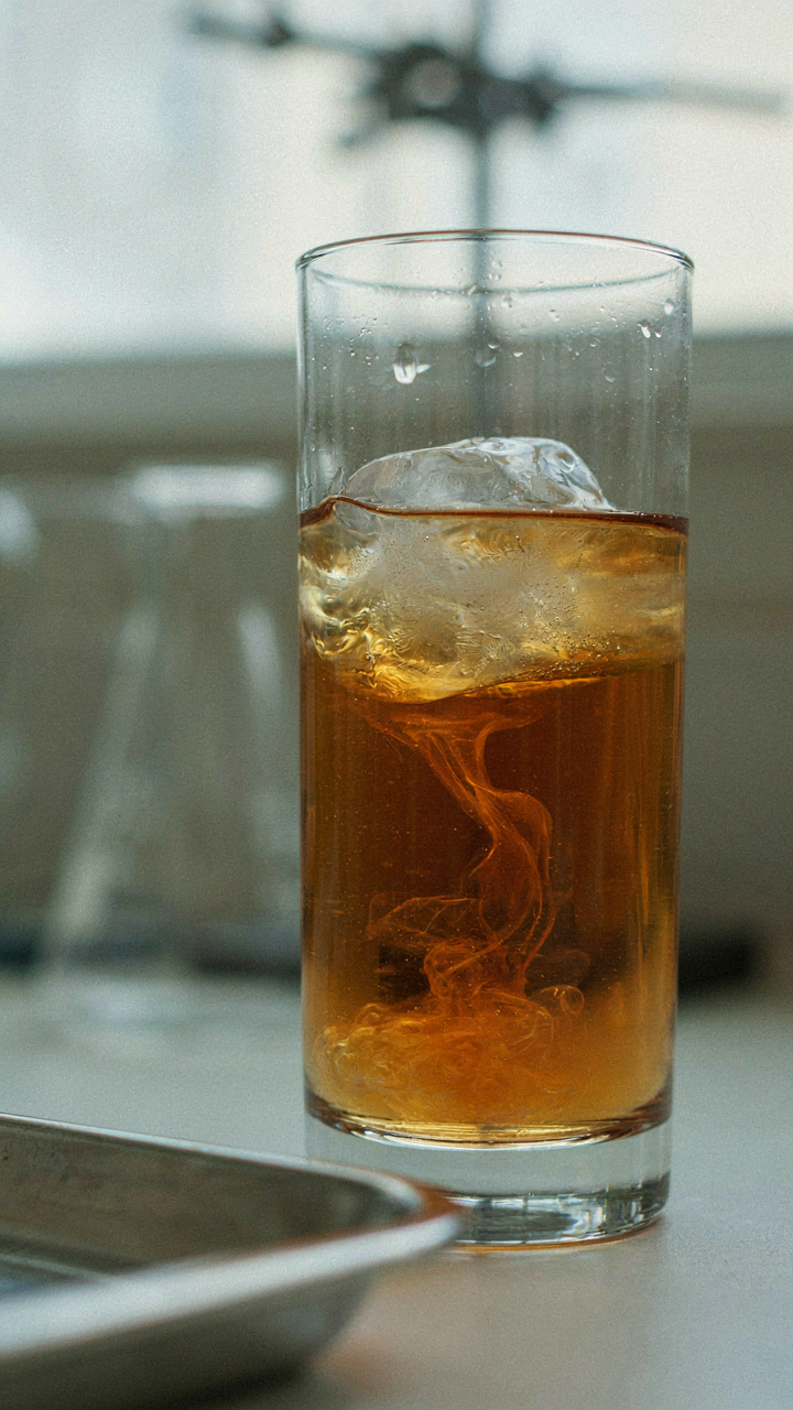 A large ice cube rapidly melts in an amber drink, showing dilution.