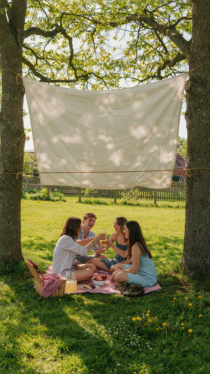 A creative DIY picnic tent made from a bedsheet gives shade to a small group.