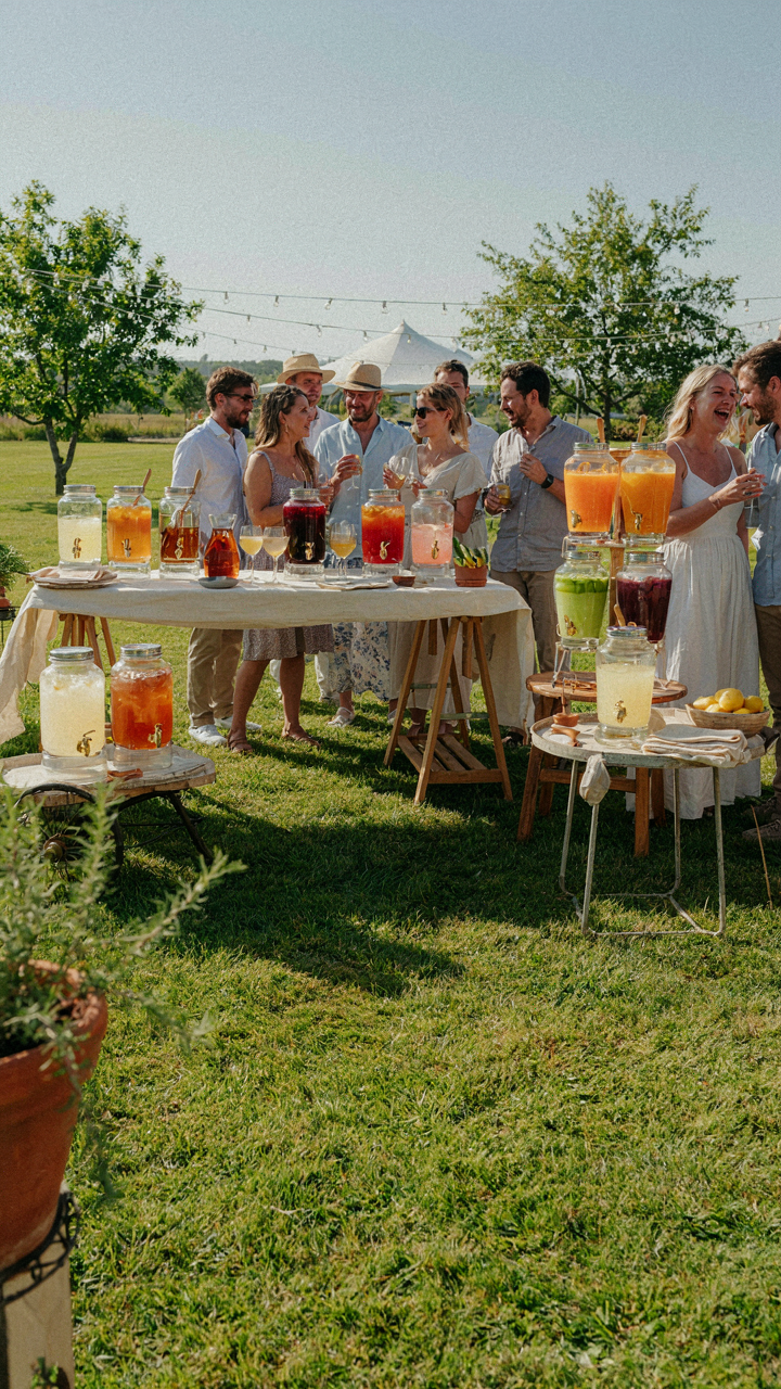 Multiple small beverage dispenser stations are scattered around an outdoor party.