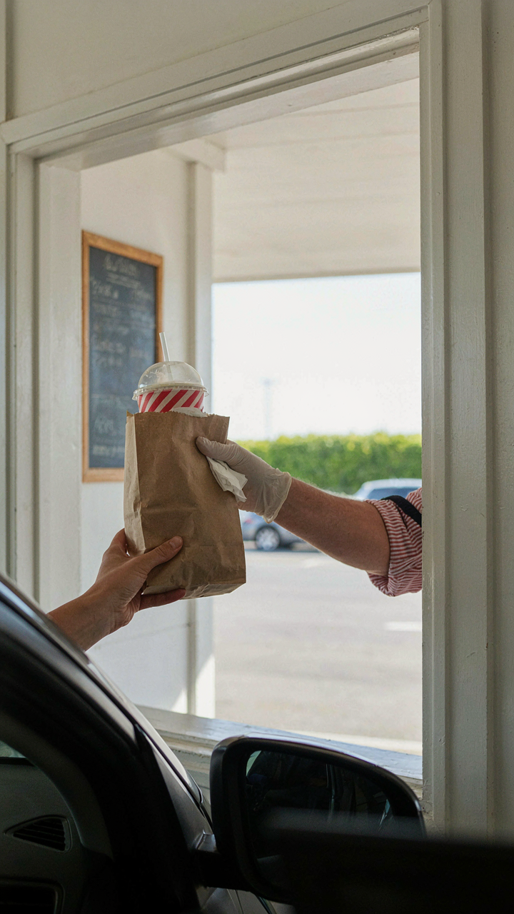A hand receives a bagged meal at a drive-thru window.