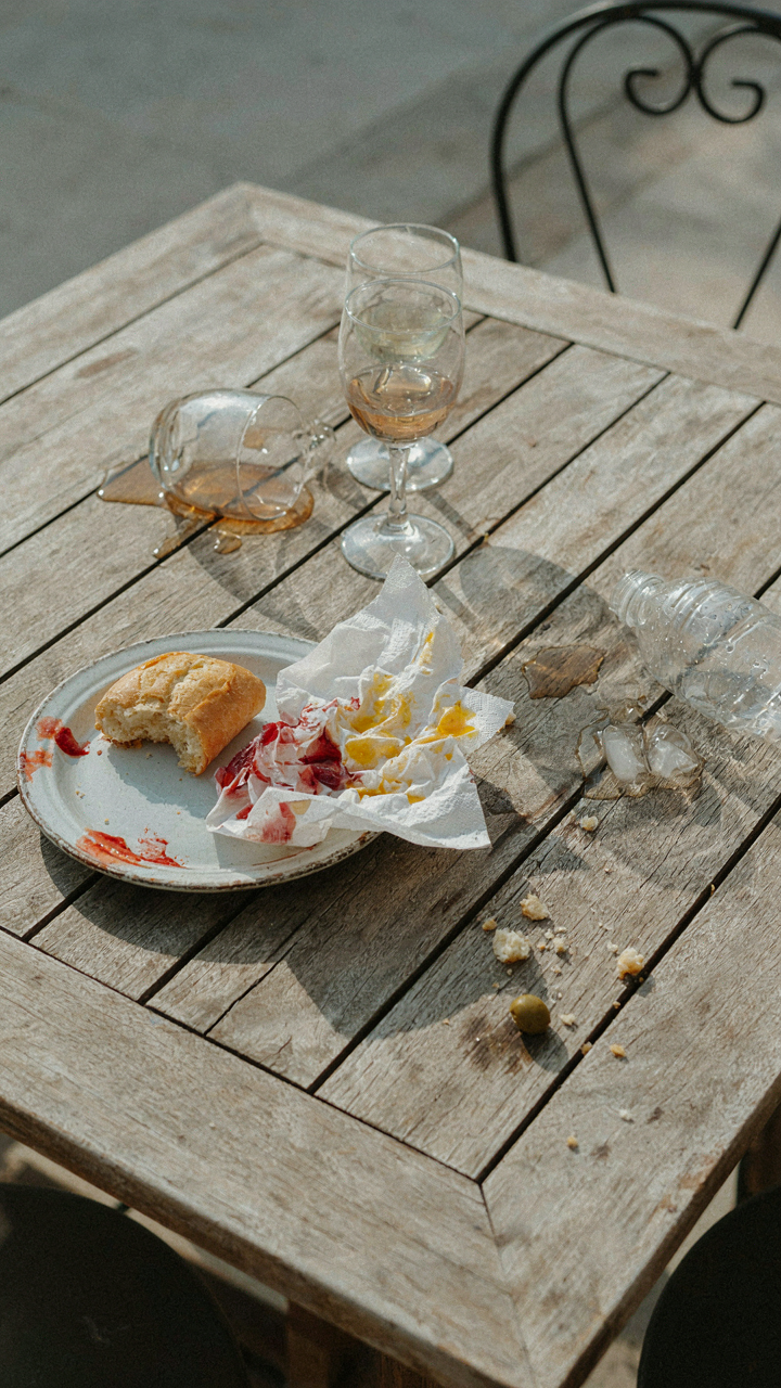 A messy outdoor table after a party, showing spilled drinks and crumpled napkins.
