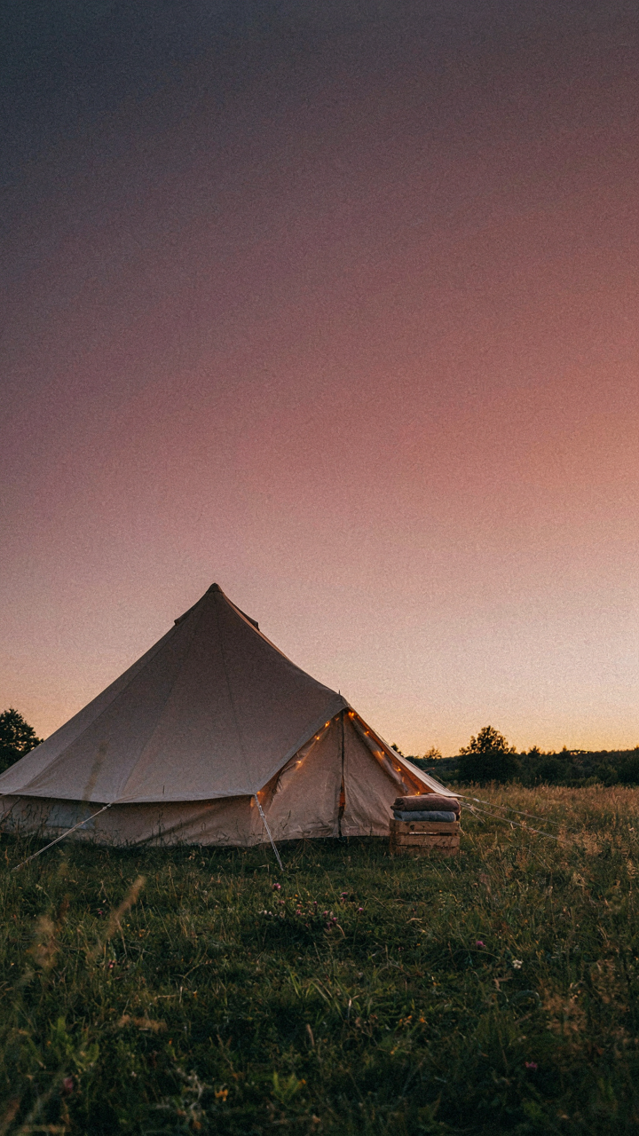 An elegantly styled canvas bell tent illuminated by decorative lights at sunset.