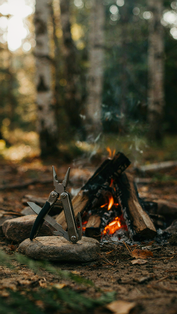 A sturdy multi-tool displayed next to a crackling campfire.