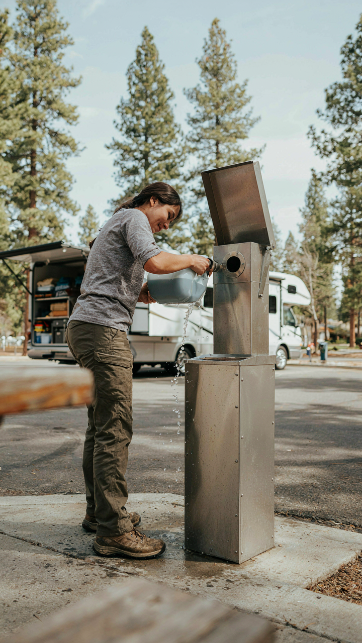 A person carefully pours gray water into a dump station at a clean campground.