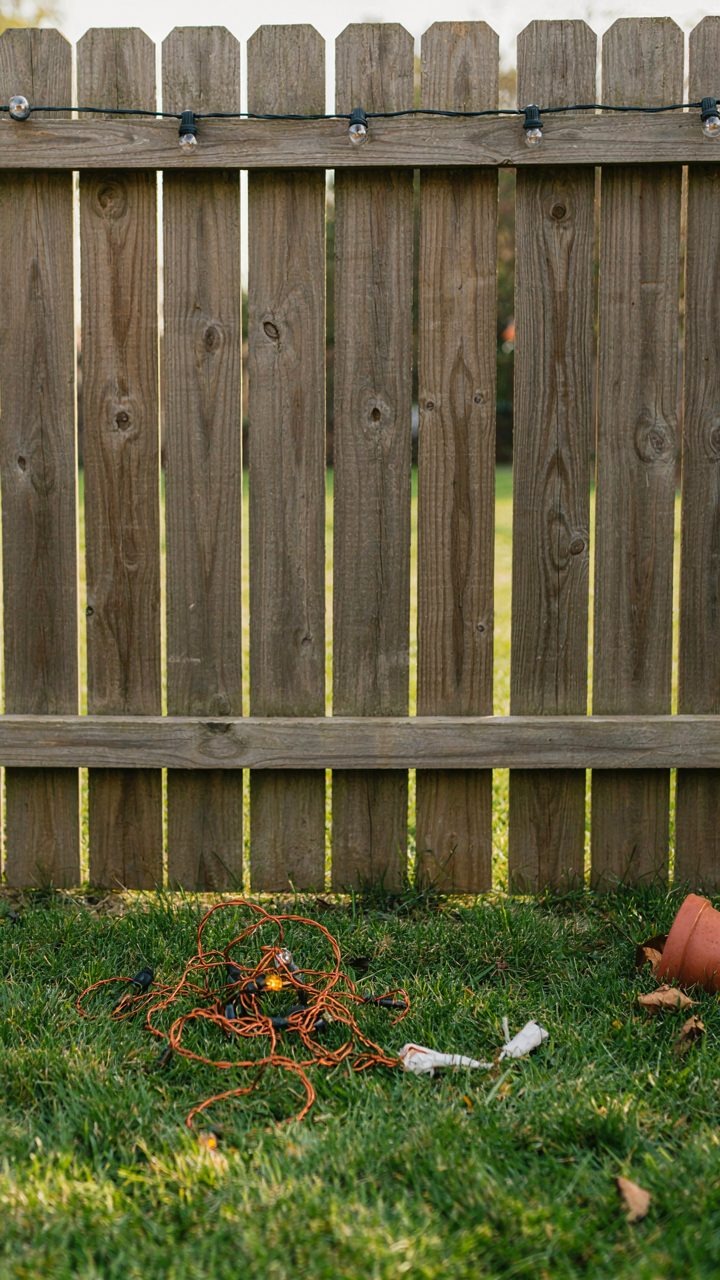 Broken, cheap fairy lights lie next to durable, working lights on a fence.