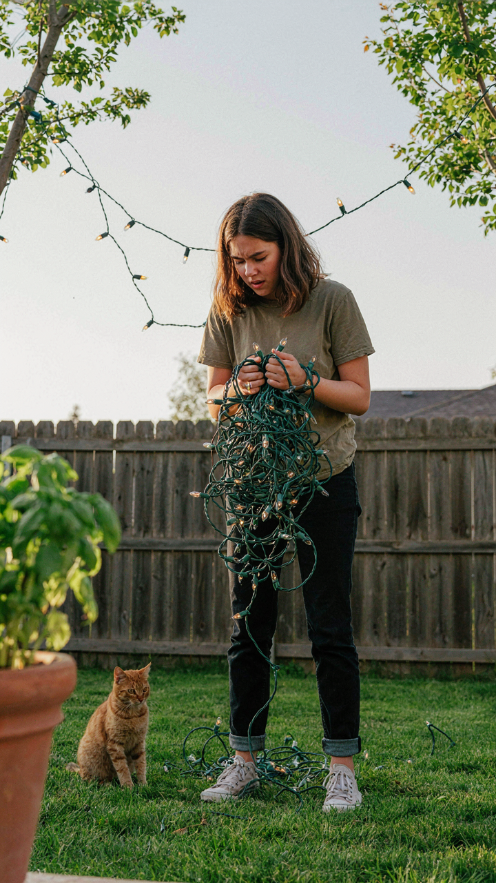 Someone struggles to untangle a large mess of string lights in a yard.