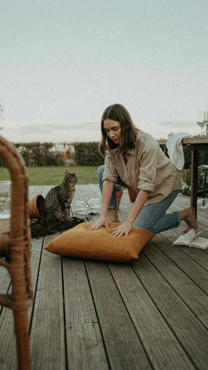 A person carefully places a cushion on a patio.
