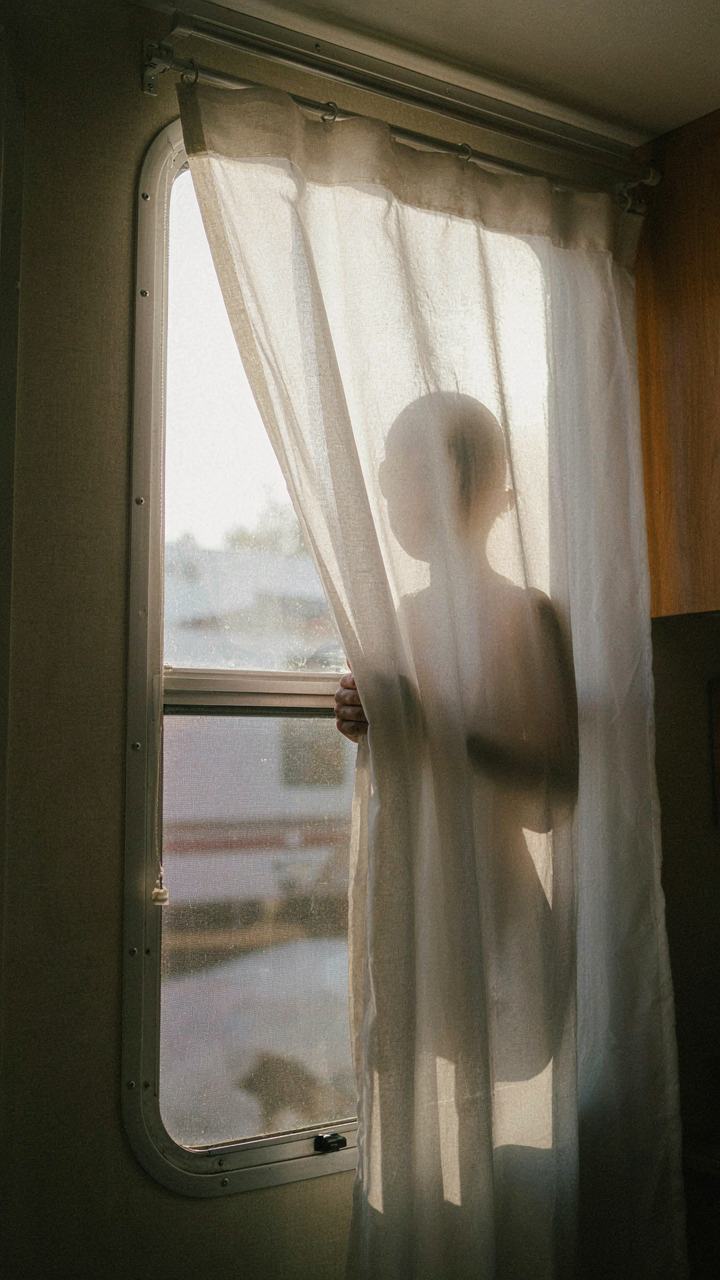 A person's shadow is seen through a thin RV curtain from outside.
