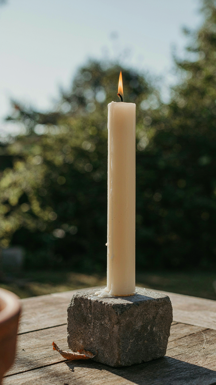 A large stone block stabilizes a tall pillar candle on a table.