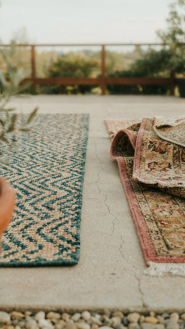 A new, good quality outdoor rug next to old, discarded rugs.
