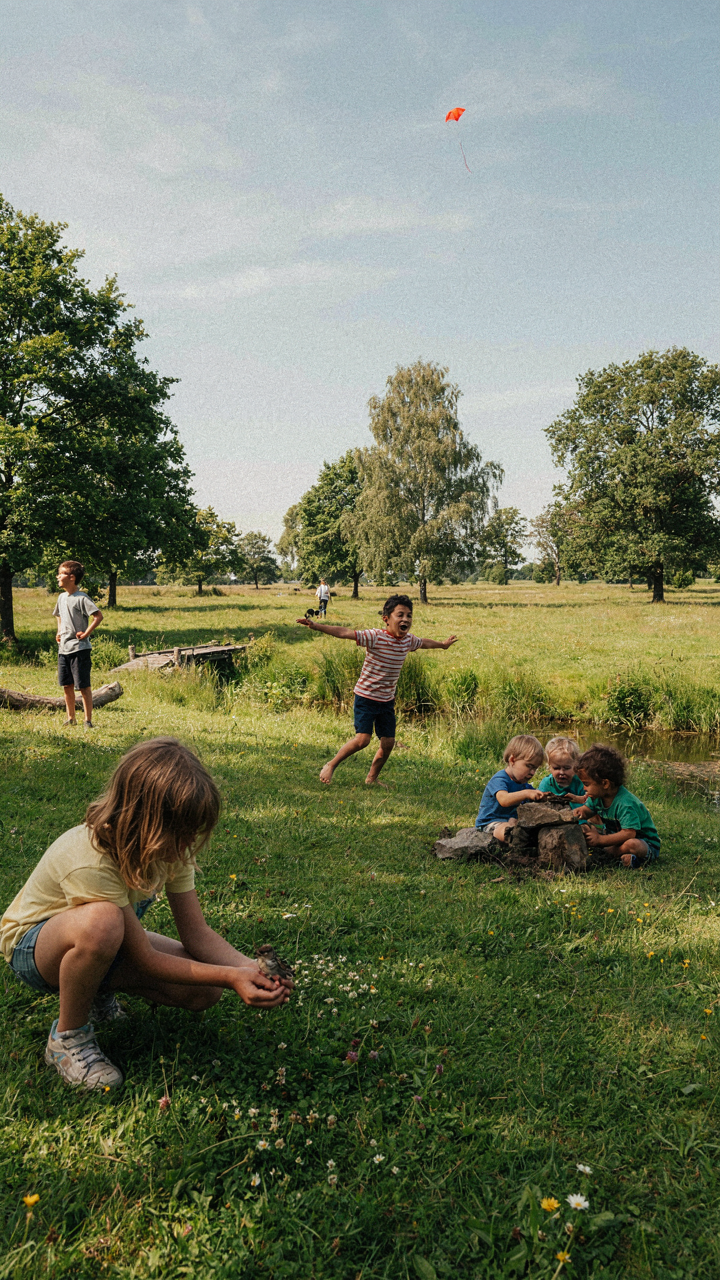 Children play freely and imaginatively in a wide, open grassy field.