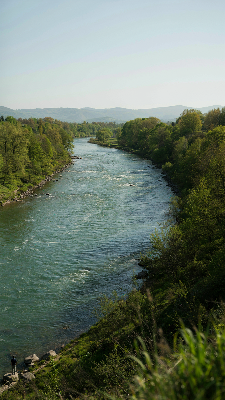 A wide river flows through a valley with a small person on the bank.