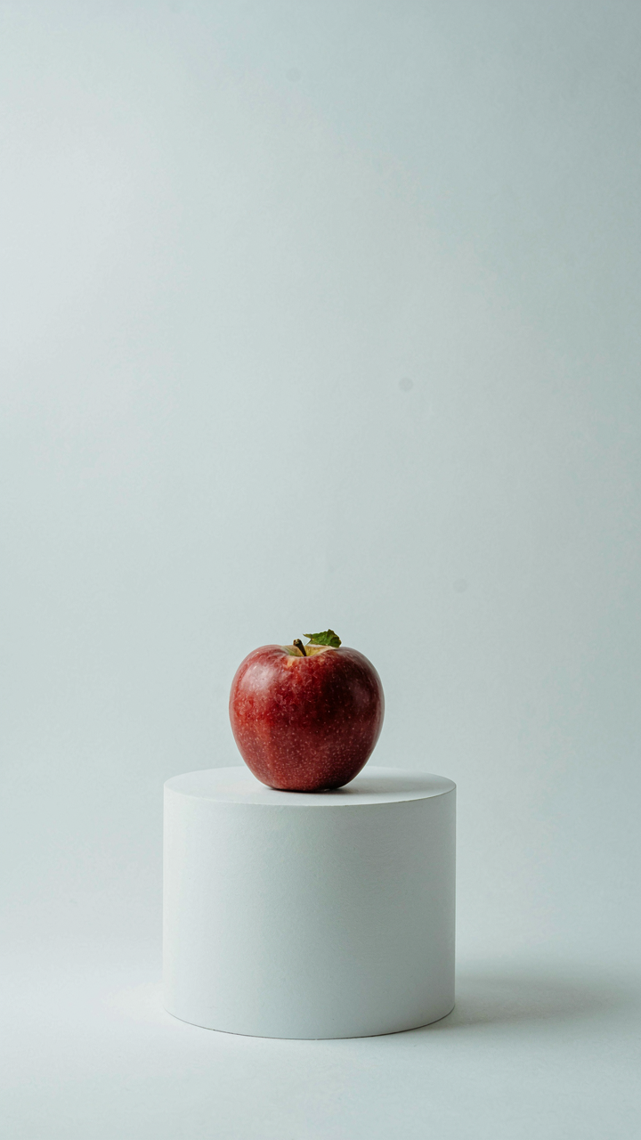 A single, perfectly ripe apple rests elegantly on a minimalist white pedestal.