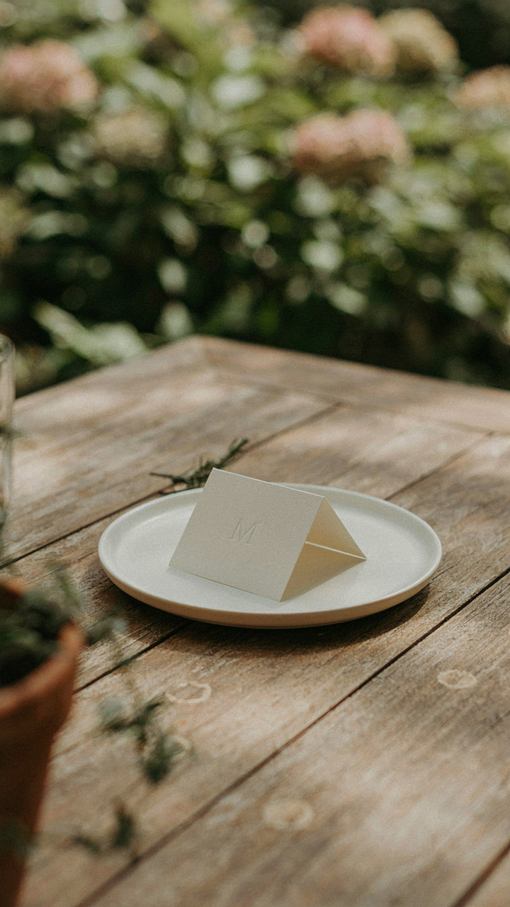 A white plate has a simple outdoor dinner place card with just one letter.