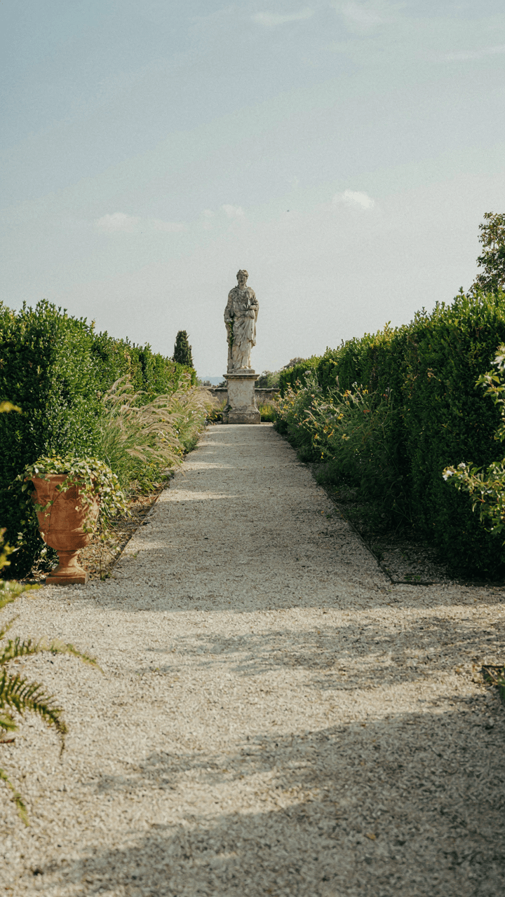A long, narrow garden path leads to a striking statue.