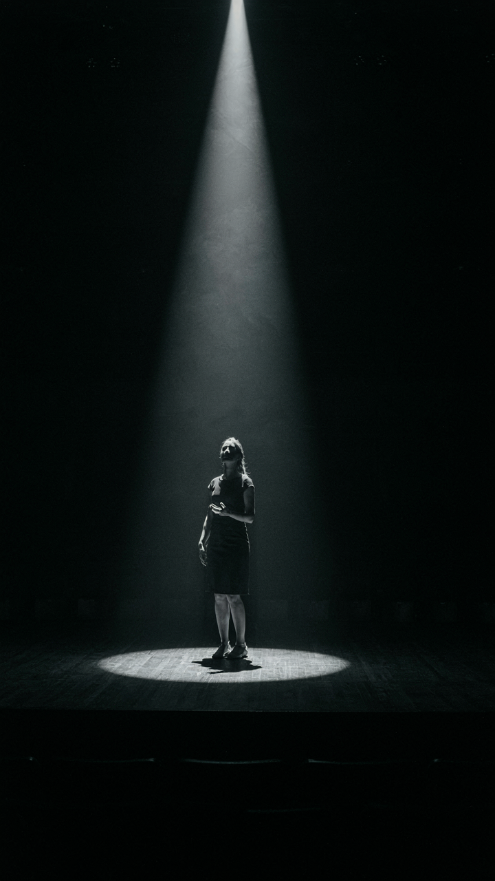 A narrow spotlight illuminates only one person on a dark stage.