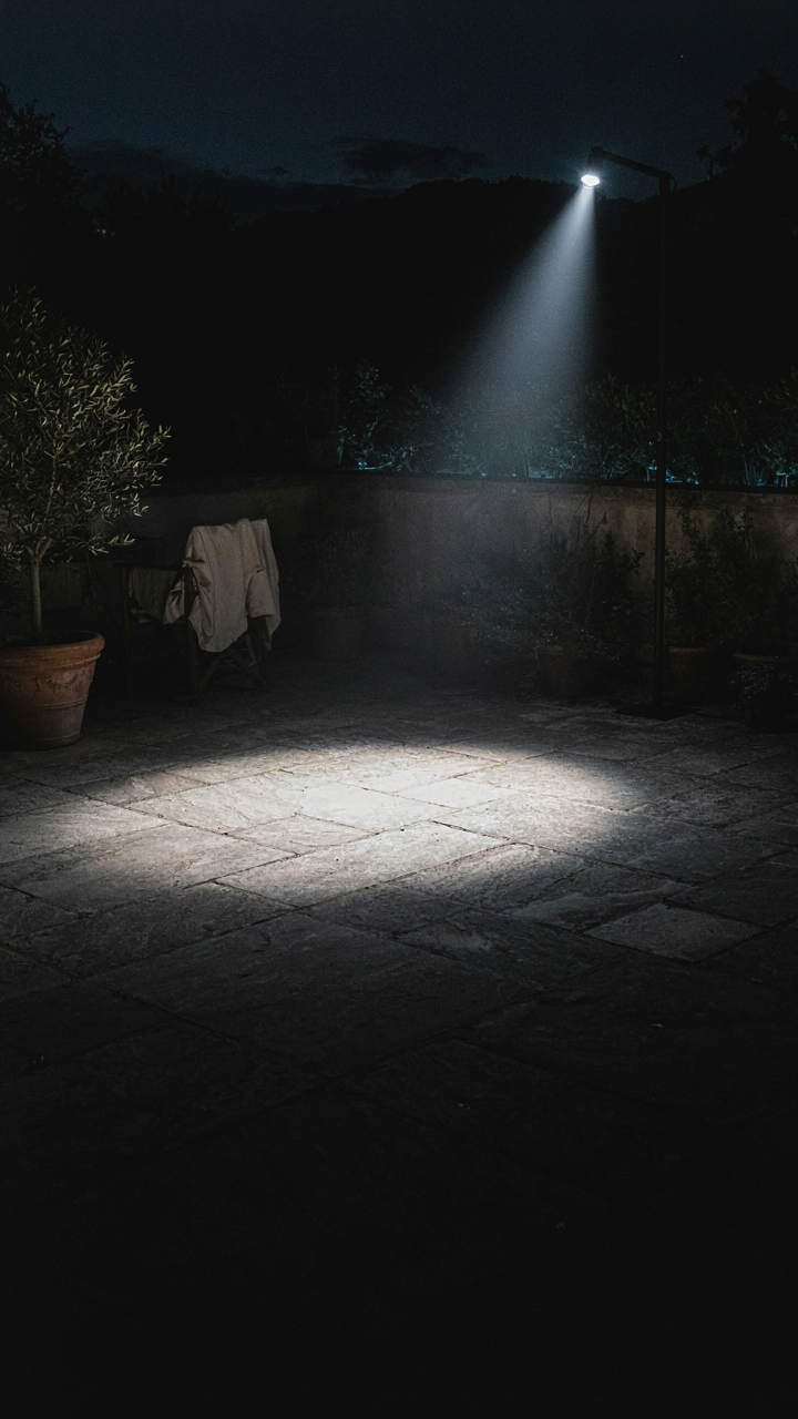 A single bright spotlight creates harsh light and deep shadows on a patio.