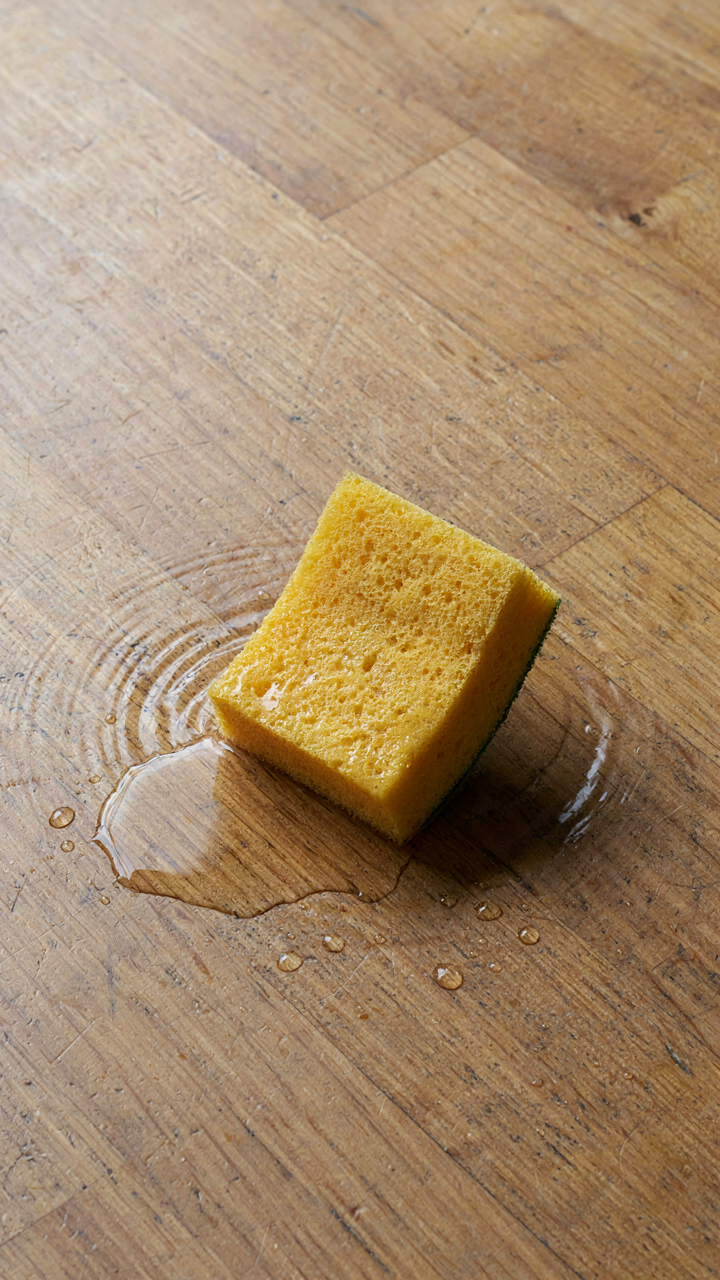 A sponge soaks up water from a puddle on a wooden floor.