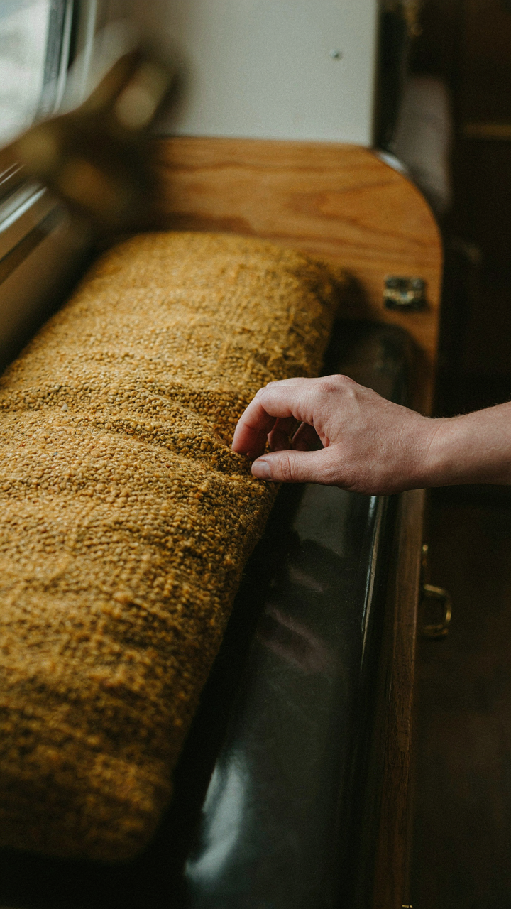 A hand touching a textured fabric cushion in a vintage camper interior.