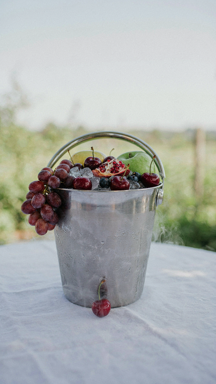Grapes and cherries sit in an ice bucket on a white tablecloth.