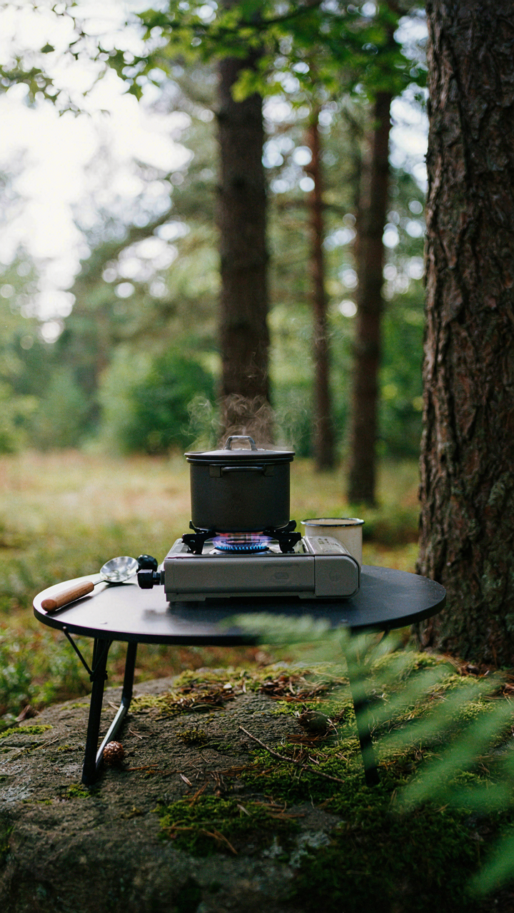 A single camping pot boils water on a compact gas stove with two utensils nearby.