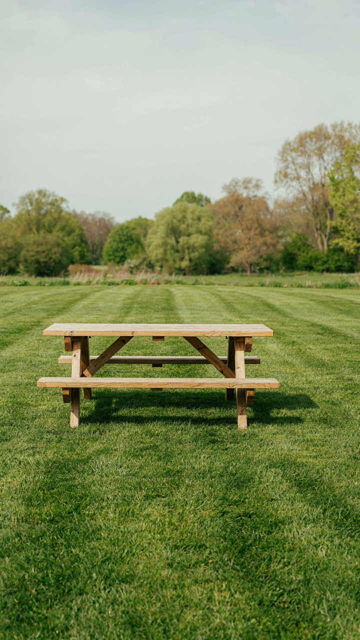 A solitary, simple wooden low table picnic table sits on a green lawn.