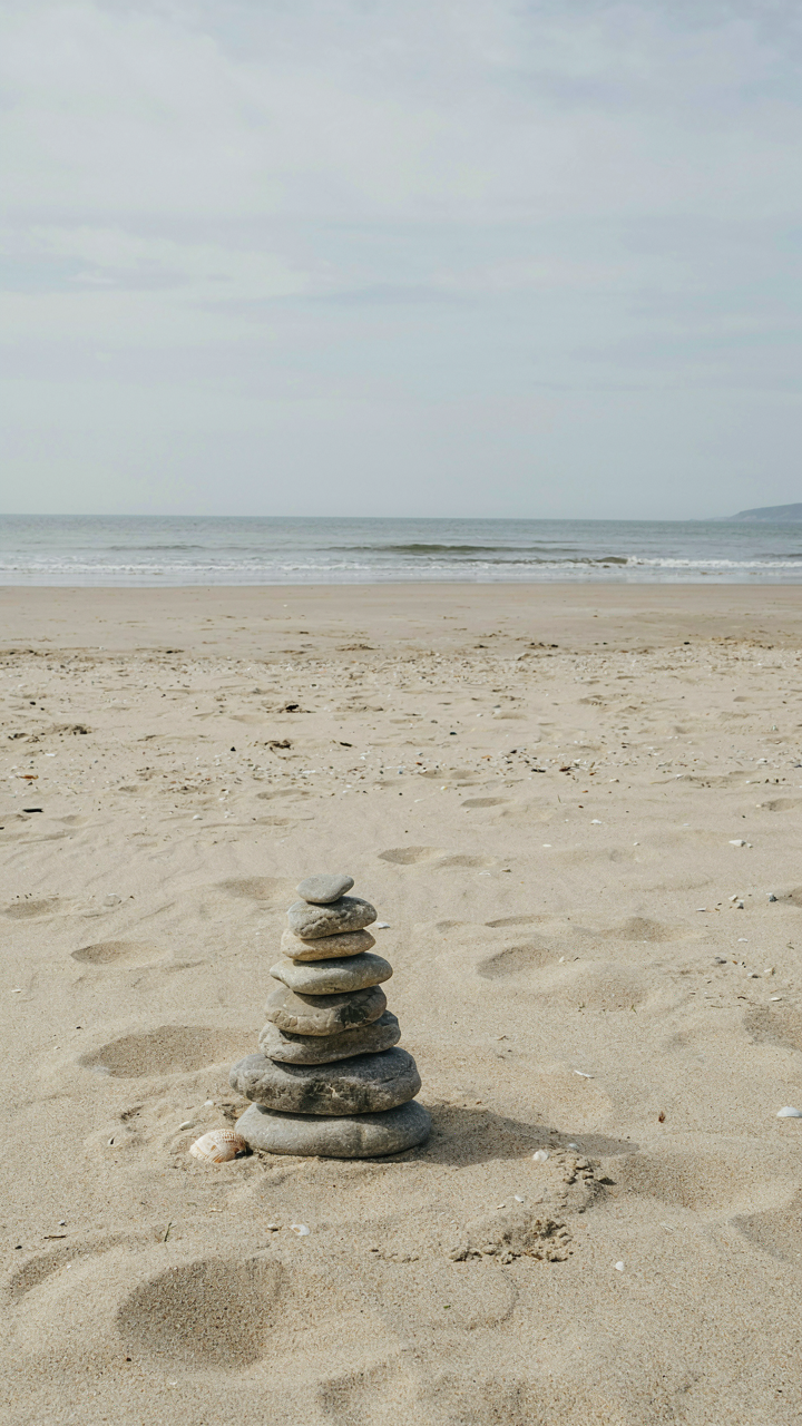 A small, perfectly balanced rock cairn on a sandy beach.