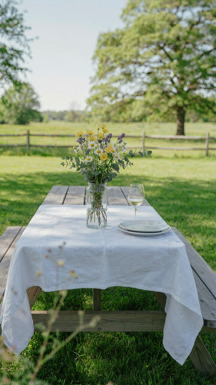 A simple wooden picnic table with a white tablecloth and wildflowers.