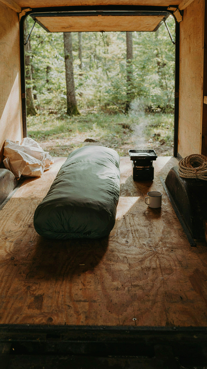 A small utility trailer camper conversion with a simple bed and stove.