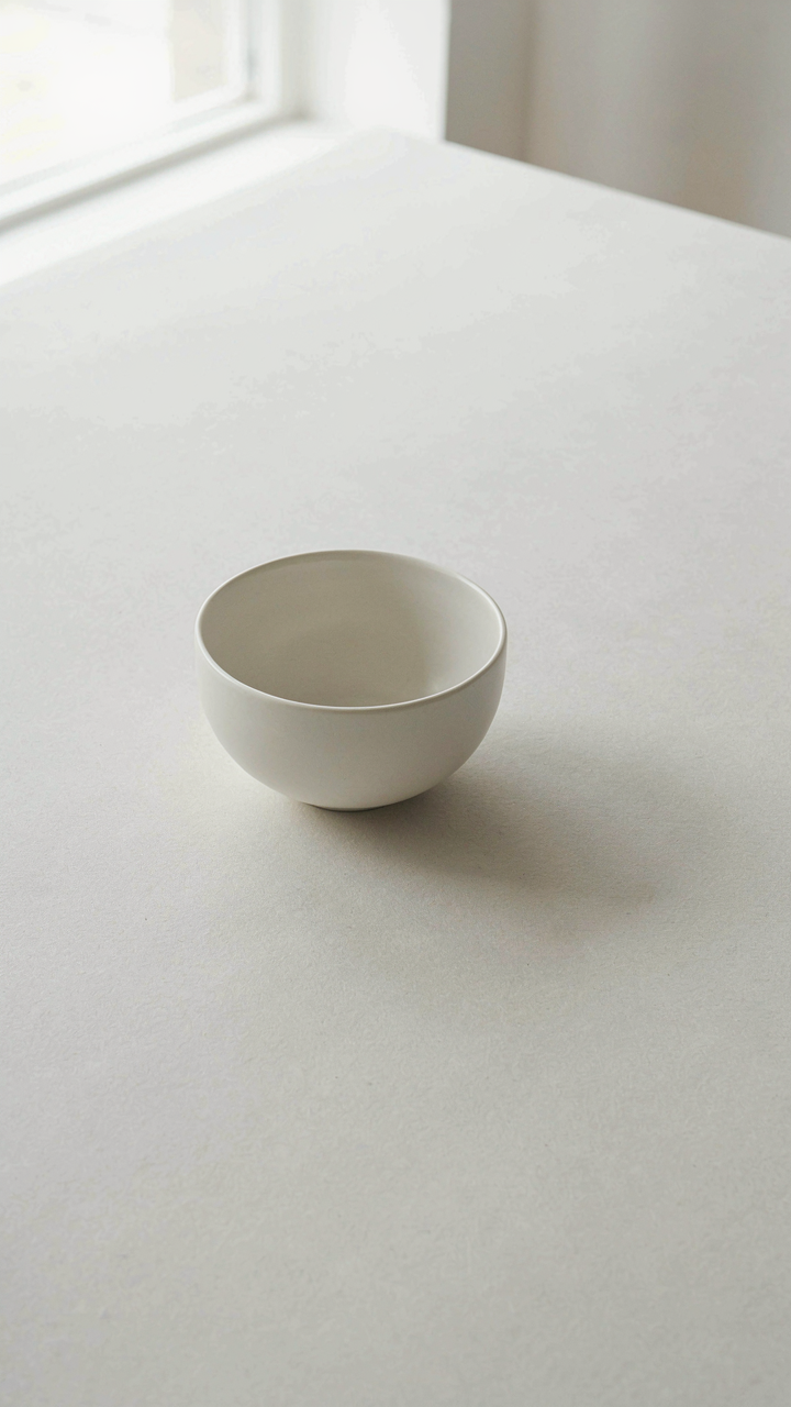 A single white bowl sits on a large, empty white table.
