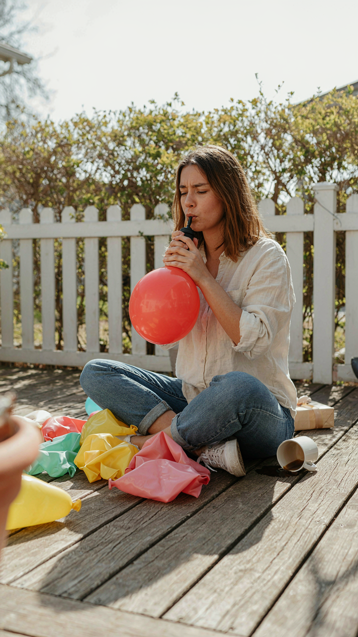A person struggles to inflate a balloon with a small pump on a patio.