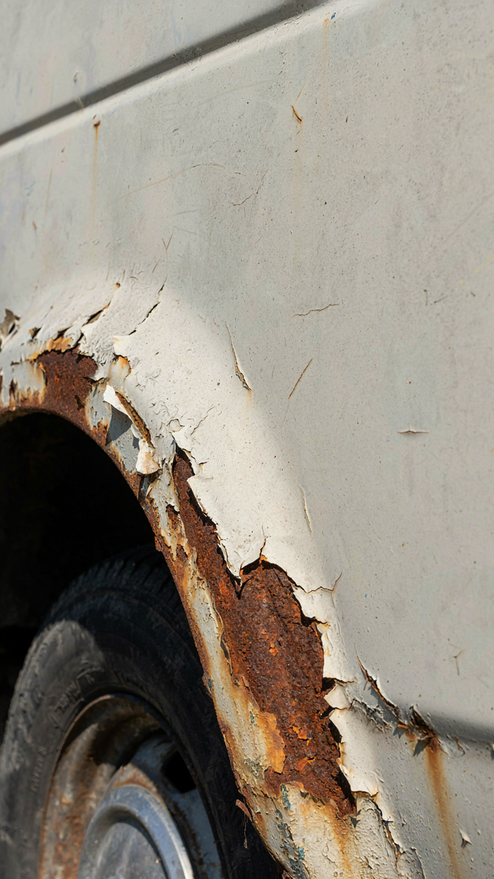 Severe rust on the wheel well of an old white van.