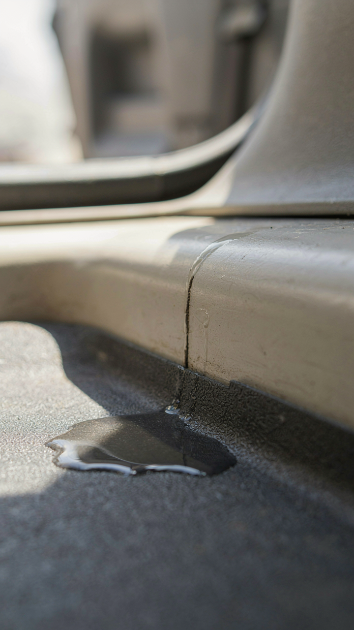 A small puddle of water seeps through a crack in a van's floor joint.