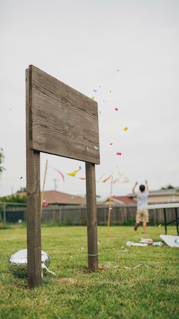 A heavy wooden sign stands strong next to broken party items in the wind.