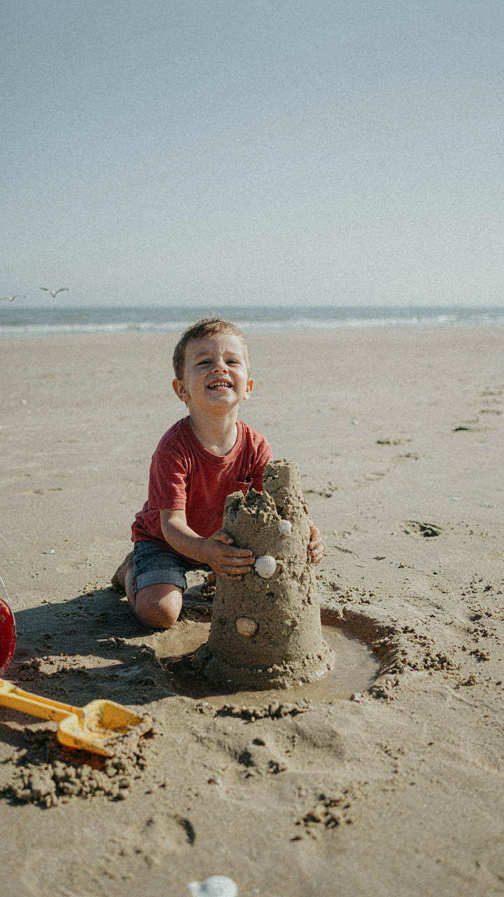 A child's imperfect sandcastle stands proudly on the beach.