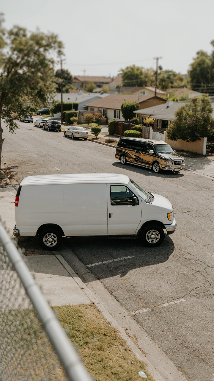 A simple white cargo van is parked near an ornate luxury van.