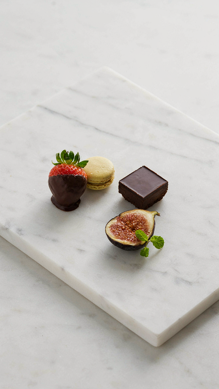 A minimalist dessert charcuterie board with five items on a marble slab.