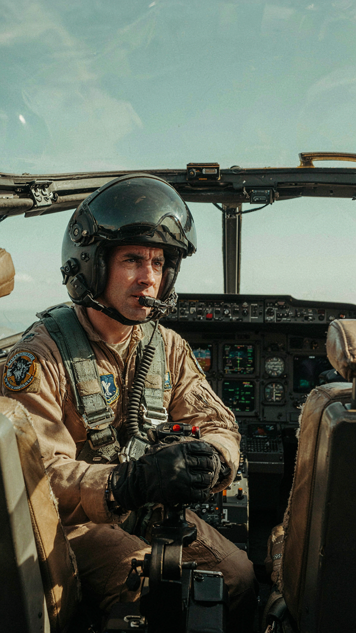 A fighter pilot observing instruments and moving controls in a cockpit.