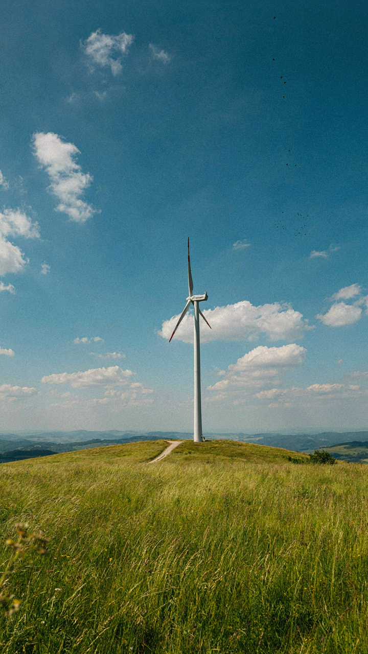 A large wind turbine spins quickly on a hill under a bright sky.