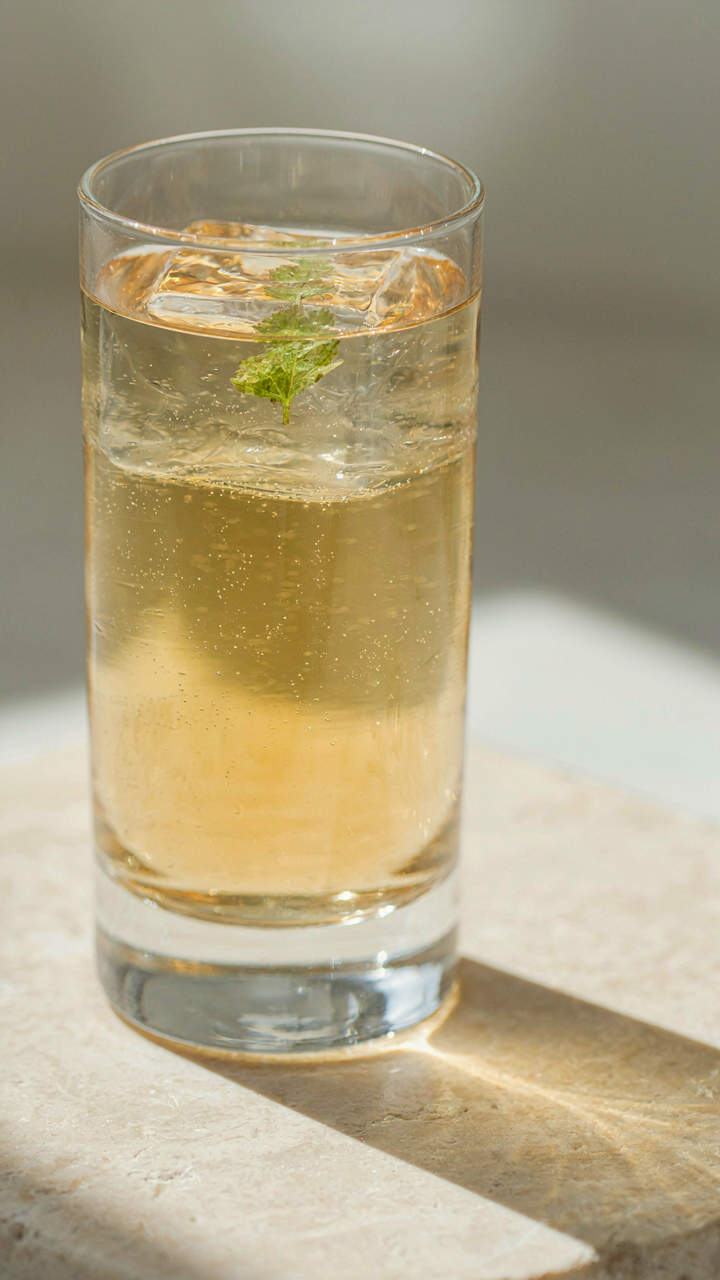 A clear ice cube with a single herb leaf in a simple cocktail.