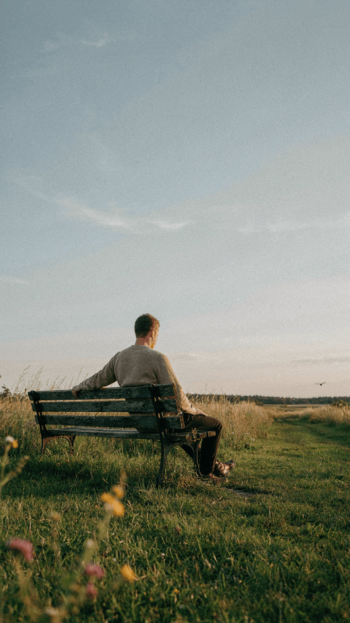 A person sits alone on a park bench, thinking.