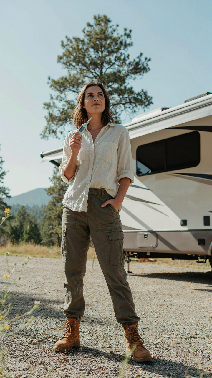 A person stands confidently by an RV, holding a thermometer showing a comfortable temperature.