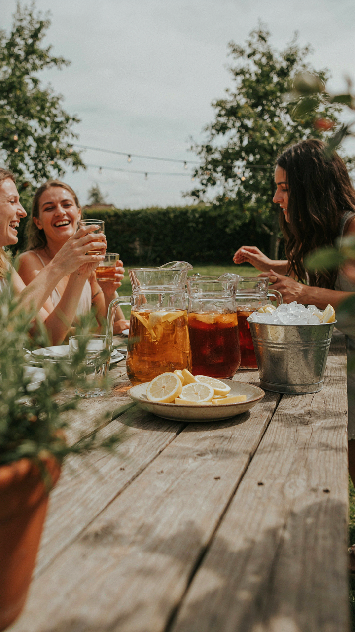 A simple iced tea bar with three pitchers, lemon, and ice, with happy guests.