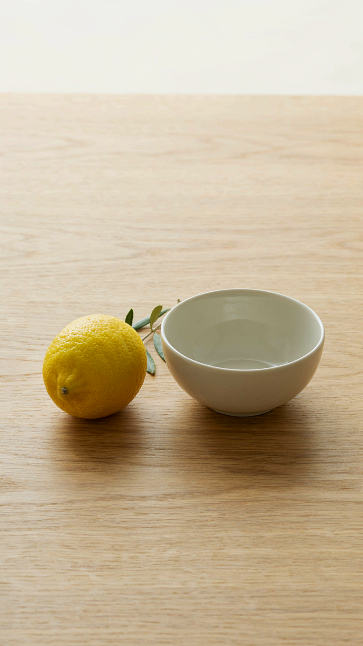 A minimalist composition with a lemon, an olive sprig, and a ceramic bowl.
