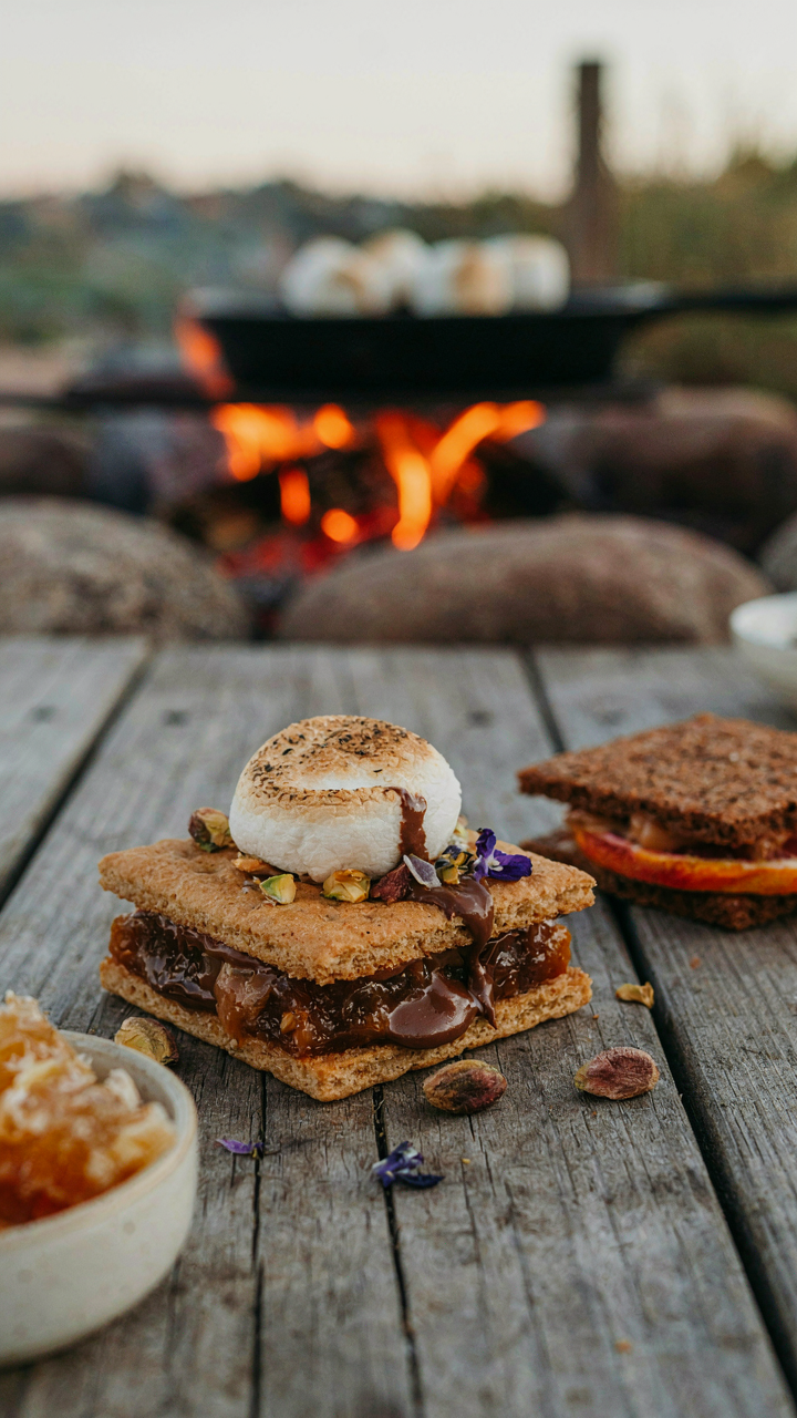 A unique s'mores with special ingredients is ready by a fire pit.