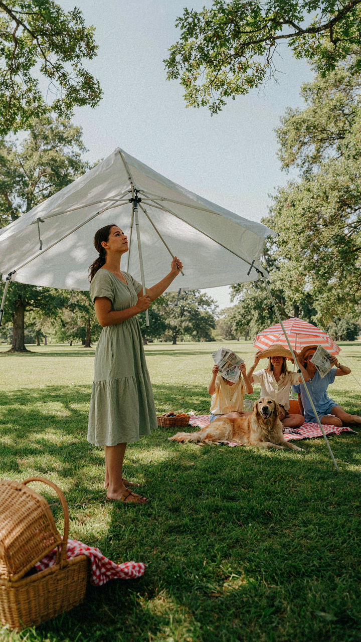 A person sets up a pop-up picnic canopy while others struggle in the sun.