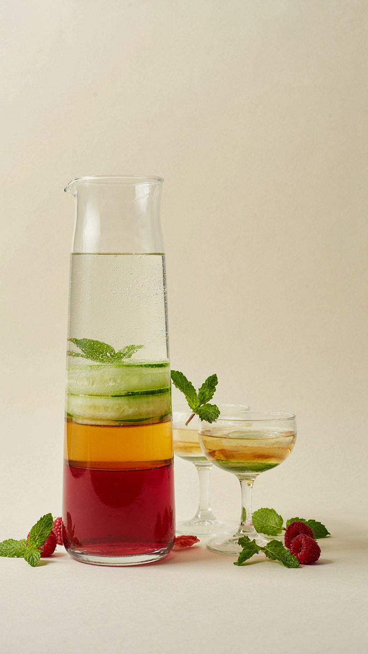 A sophisticated, layered mocktail pitcher shows distinct bands of colored liquids.